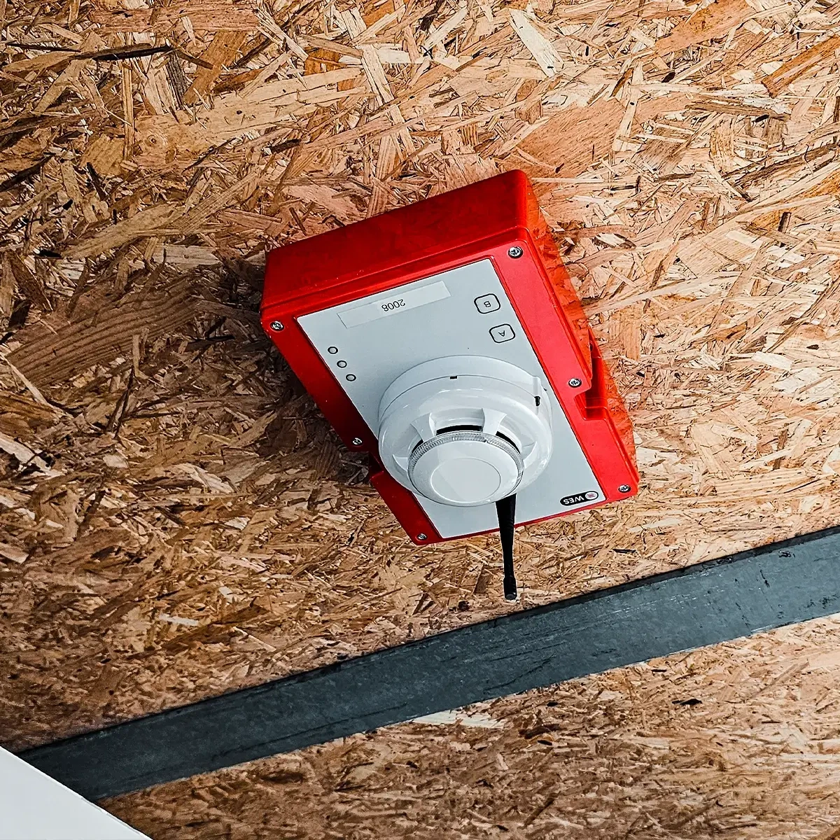 Détecteur de fumée sans fil WES3 rouge monté sur un plafond en panneau OSB dans un paddock temporaire