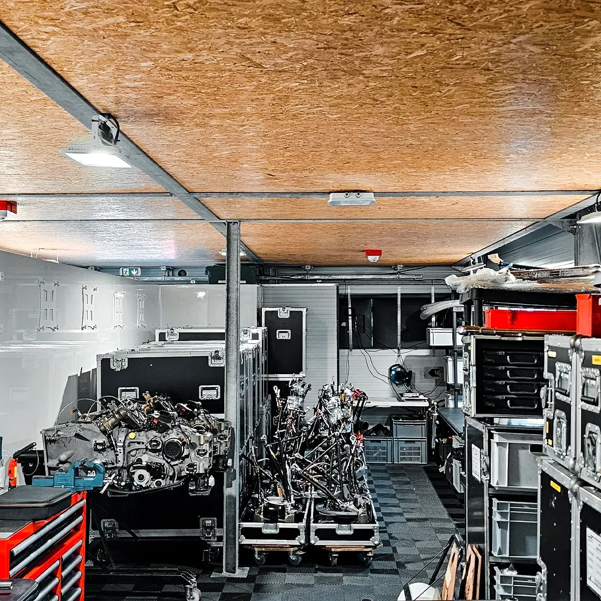 Intérieur d'un paddock d'équipe du Mans avec des moteurs de course et de l'équipement sous des détecteurs fixés au plafond