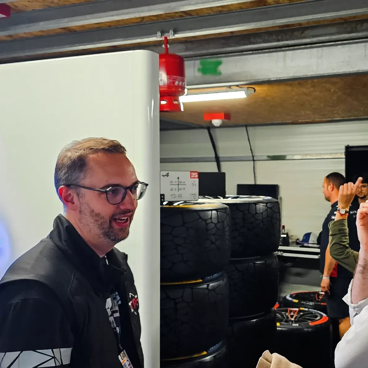 Trois personnes discutant à l'intérieur d'un paddock du Mans avec des détecteurs WES3 visibles au plafond