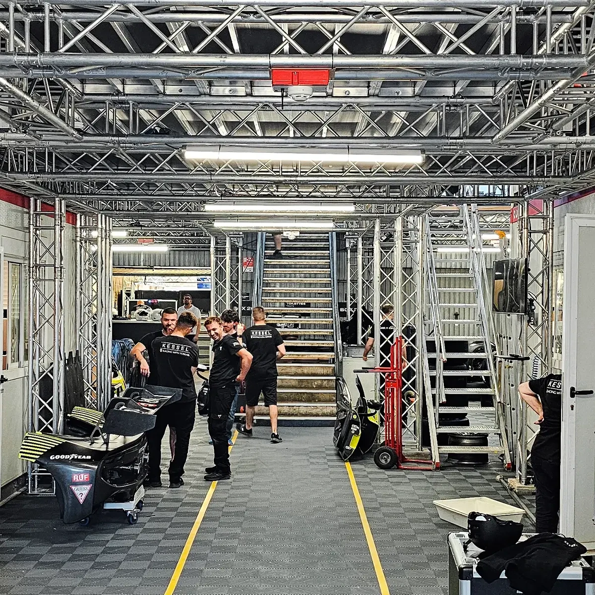 Structure temporaire de paddock avec échafaudages et fermes au Mans avec des membres d'équipes de course travaillant en dessous
