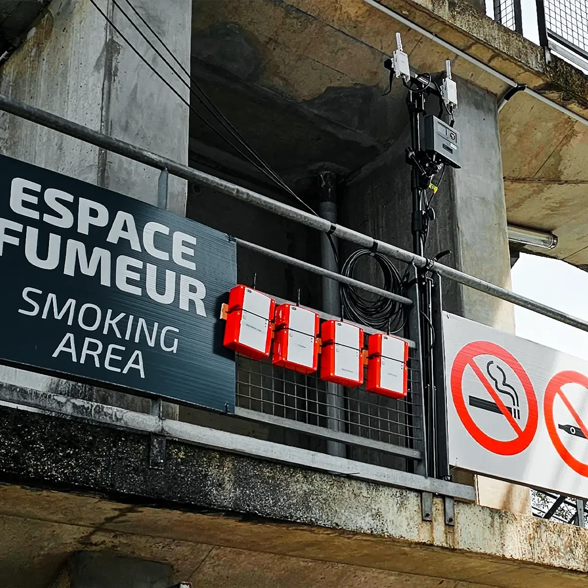 Quatre unités sans fil WES3 rouges montées sur des garde-corps à côté d'un panneau de zone fumeurs au Mans
