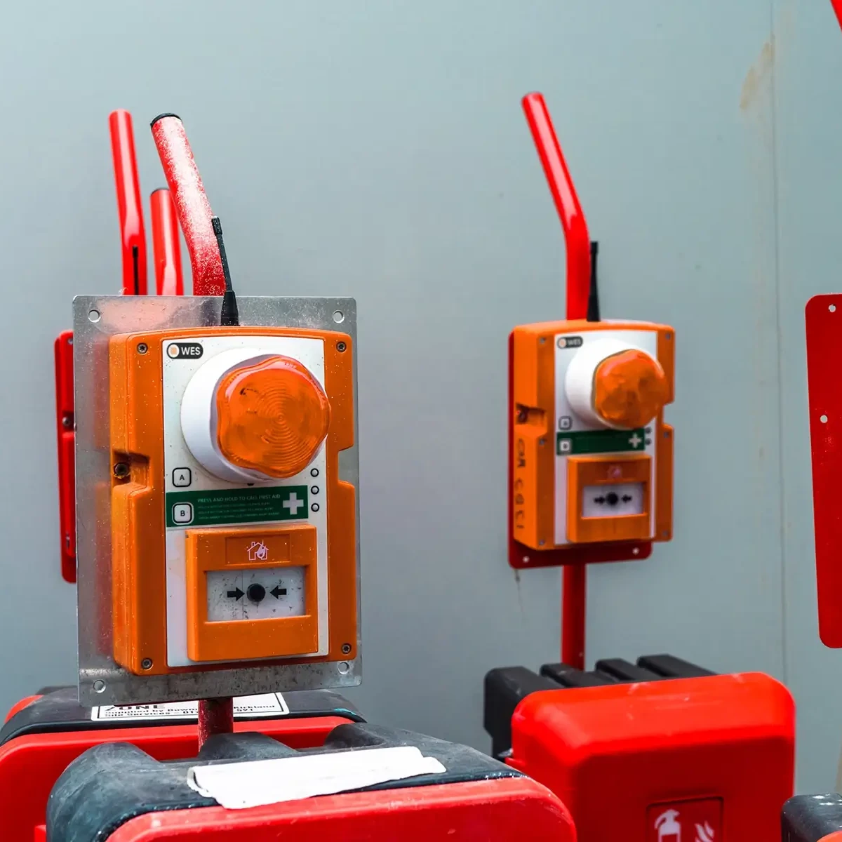 Orange WES wireless fire and evacuation call points mounted on red mobile fire safety units at construction site.