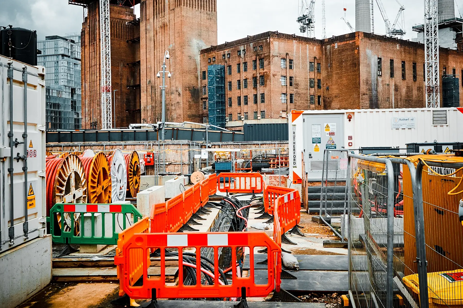 Construction staging area with large cable spools, orange safety barriers, and site containers for the Northern Line Extension Fire Safety.